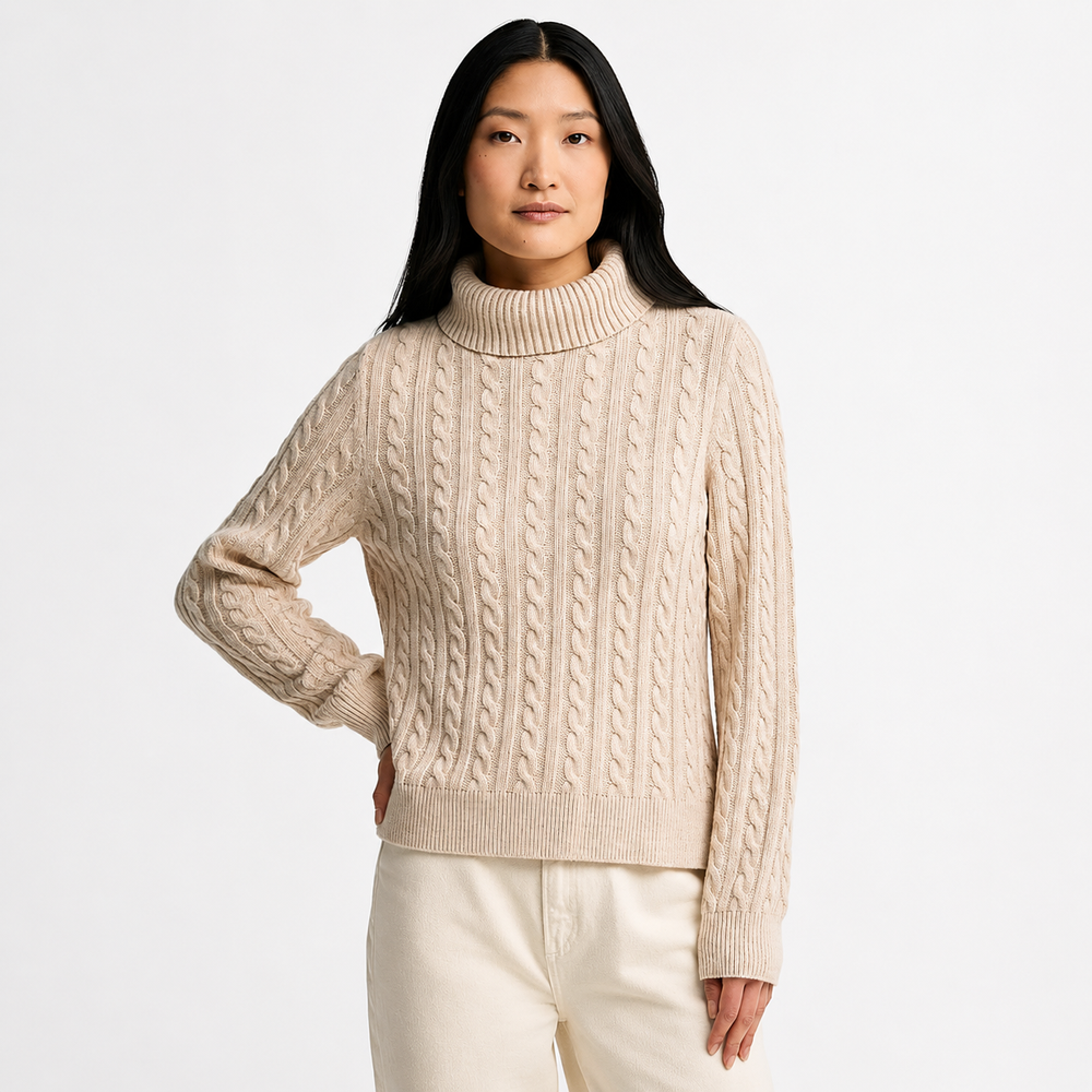 A woman wearing a cream-colored cable-knit turtleneck sweater and matching cream pants, photographed against a clean white studio background.
