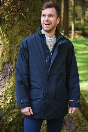 A man wearing a dark navy blue hooded jacket stands outdoors in front of a mossy tree, smiling and looking to the side.
