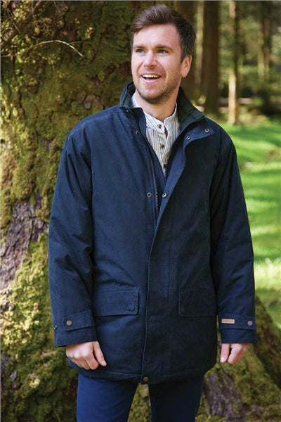 A man wearing a dark navy blue hooded jacket stands outdoors in front of a mossy tree, smiling and looking to the side.