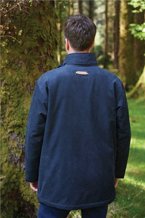 A man viewed from behind wearing a dark navy blue jacket in a forest setting.