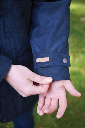 Close-up of a person's hands adjusting the cuff of a dark navy blue jacket outdoors, with a small tan rectangular patch and a metal snap button visible on the sleeve.