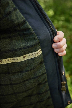 Close-up of a person's hand holding open a dark navy zipper on a green plaid wool jacket, showing the Lee Valley label.