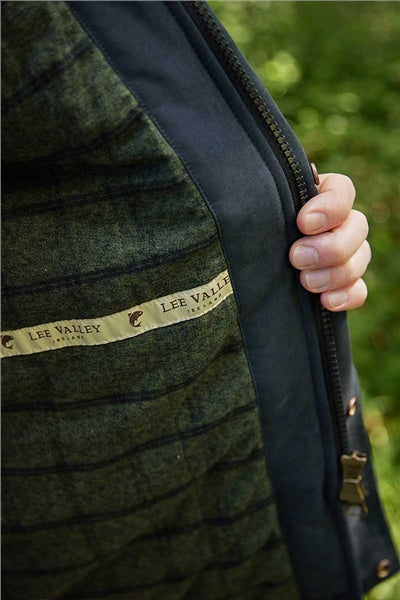 Close-up of a person's hand holding open a dark navy zipper on a green plaid wool jacket, showing the Lee Valley label.