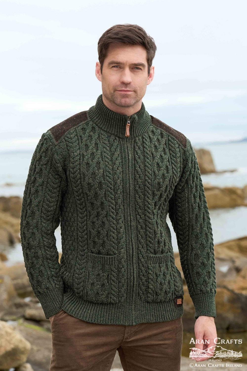 Man wearing a green knitted sweater with brown accents by a coastal background
