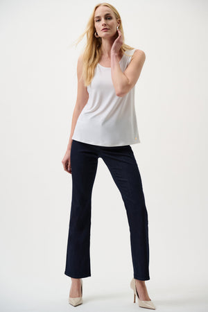 Woman wearing a white sleeveless top and dark pants on a white background