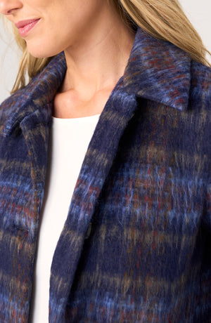 Close-up of a woman wearing a textured, fuzzy plaid coat in navy blue with red and brown accents over a white top.