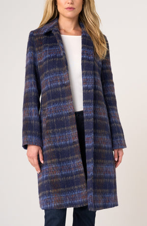 A woman wearing a long open-front coat with a textured blue, navy, and brown plaid pattern over a white top and dark pants, photographed against a plain light background.