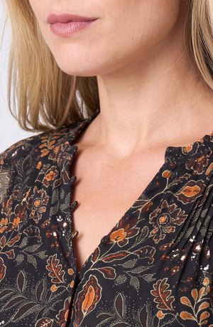Close-up of a woman wearing a black blouse with a brown and orange floral pattern and scalloped neckline.