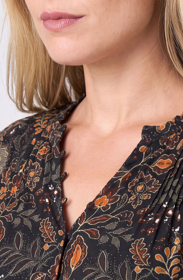 Close-up of a woman wearing a black blouse with a brown and orange floral pattern and scalloped neckline.