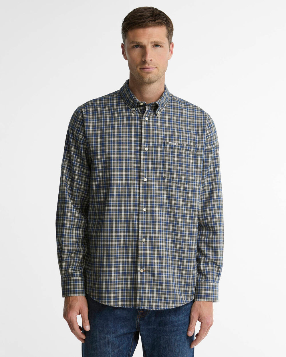 A man wearing a long-sleeve button-down plaid shirt in blue, beige, and white, paired with dark blue jeans, standing against a light gray studio background.