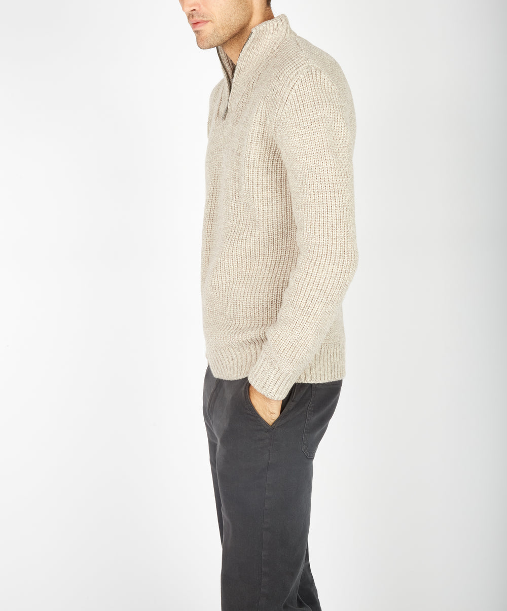 Man wearing a beige knitted sweater and dark pants on a white background