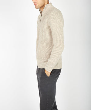 Man wearing a beige knitted sweater and dark pants on a white background