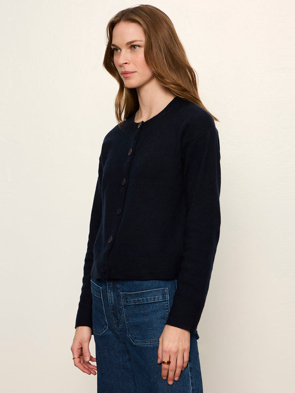 A woman modeling a dark navy blue long-sleeve button-up cardigan sweater paired with blue jeans, photographed against a plain off-white studio background.