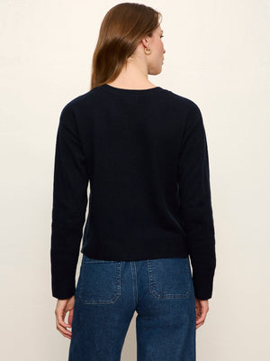 A woman viewed from the back wearing a dark navy long-sleeve knit top and blue jeans against a plain off-white background.