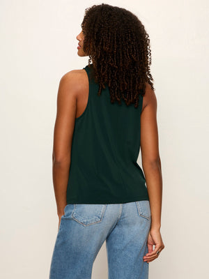 A woman shown from the back wearing a dark green sleeveless tank top and light blue jeans, photographed against a plain off-white studio background.
