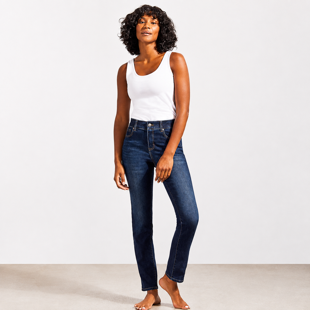 A woman modeling a pair of dark blue skinny jeans with a white tank top, standing barefoot against a clean white studio background.