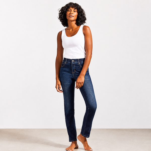 A woman modeling a pair of dark blue skinny jeans with a white tank top, standing barefoot against a clean white studio background.