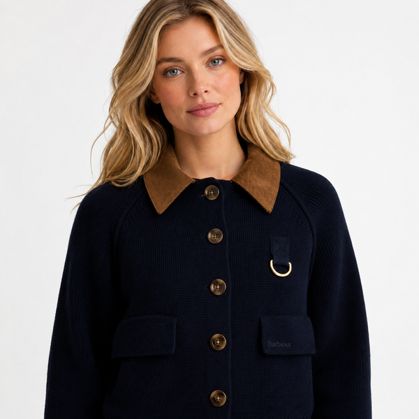 A woman wearing a dark navy ribbed knit jacket with a brown corduroy collar, brown buttons, and a gold-tone D-ring detail on the chest pocket, photographed against a clean white studio background.
