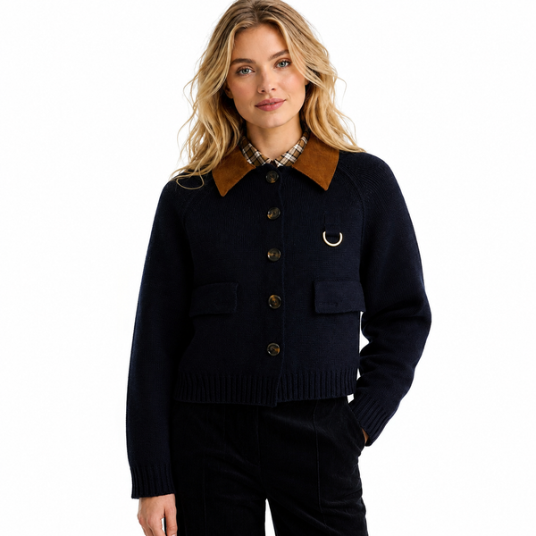 A woman modeling a dark navy knit cardigan with a brown corduroy collar, brown buttons, flap pockets, and a small gold ring detail on the chest, paired with dark pants against a plain white background.