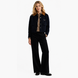 A woman models a dark navy jacket with a brown corduroy collar, paired with black wide-leg trousers, a brown and beige plaid shirt, and black shoes, against a plain white studio background.