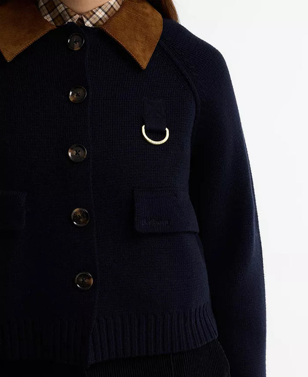 Close-up of a navy knit cardigan with a brown corduroy collar, dark buttons, flap pockets, and a gold-tone ring detail on the chest.