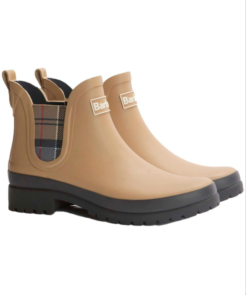 A pair of beige rubber rain boots with black soles and a plaid elastic side panel. The boots feature a white square logo patch on the side with the brand name 'Barbour' partially visible.