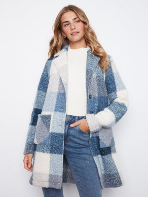A woman wearing a blue and white plaid fuzzy teddy coat over a white top and blue jeans, standing against a plain white studio background.