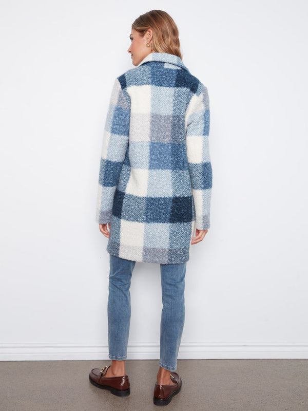 A woman shown from the back wearing a blue and white plaid fuzzy coat, blue jeans, and brown loafers, standing against a plain white wall.