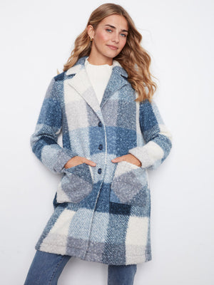 A woman wearing a blue and white plaid fuzzy coat over a white top and blue jeans, standing against a plain white background.