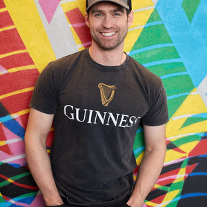 Man wearing a black Guinness t-shirt in front of a colorful abstract mural