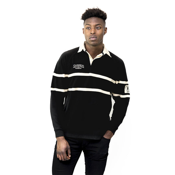 A man modeling a black long-sleeve rugby shirt with cream horizontal stripes and 'Guinness' branding on the chest, set against a plain white background.