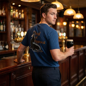 Man holding a beer in a bar wearing a blue t-shirt with a logo and text.