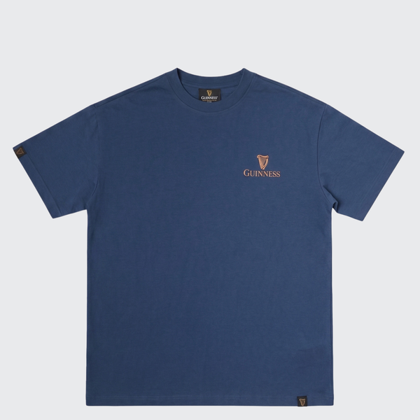 A navy blue short-sleeve crewneck t-shirt by Guinness, featuring the brand's logo and harp emblem embroidered in gold on the left chest, displayed against a light gray background.